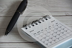 May 2023 white desk calendar with black pen on wooden table.