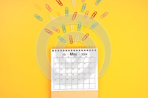 May 2024 desk calendar and colorful metal paperclips on yellow background