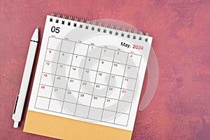 May 2024 desk calendar and pen on red background