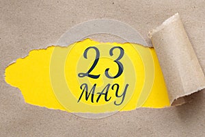 may 23. 23th day of the month, calendar date. Hole in paper with edges torn off. Yellow background is visible through