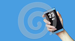 may 23. 23th day of the month, calendar date.Woman's hand holds mobile phone with blank screen on blue isolated