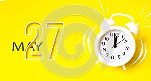 May 27th. Day 27 of month, Calendar date. White alarm clock with calendar day on yellow background. Minimalistic concept of time,