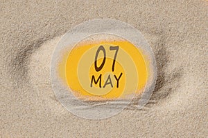 May 7. 7th day of the month, calendar date. Hole in sand. Yellow background is visible through hole