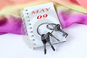 May 9 calendar: notepad with May inscription in English, number 09, bright pastel scarf, bunch of old keys, top view