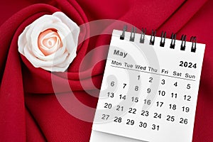 May 2024 desk calendar and pink rose on red textile