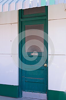 Old green REST ROOM door on dated commercial building is in good repair with white walls and awning overhang. photo