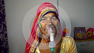 Old Indian woman infected with Covid 19 disease. Patient inhaling oxygen wearing mask with liquid Oxygen flow photo