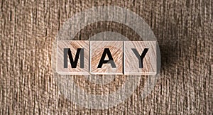 MAY is a word written on wooden cubes. On a brown background for your design, top view