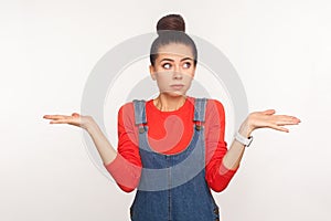 Maybe, don`t know! Portrait of clueless confused girl with hair bun in denim overalls having doubts, not sure about decision