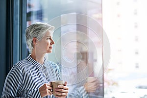 Maybe its time I went on holiday. an attractive mature businesswoman drinking coffee while looking out of her office