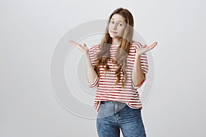 Maybe you know answer cause she clueless. Portrait of confused unaware young woman shrugging with raised spread palms