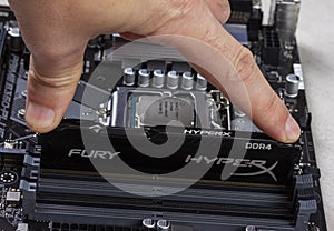 Man installs an DDR 4 DIMM 16 Gb Kingston HyperX Fury Memory RAM Module in the slot on the motherboard closeup