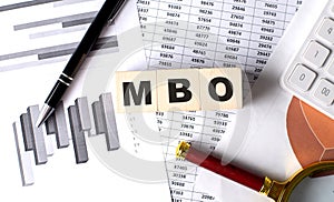 MBO text on wooden block on graph background with pen and magnifier