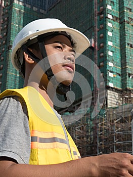 MCU Asian engineer with hardhat seen in 3/4 view, with construction in background