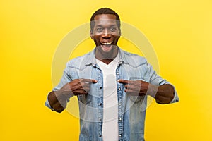 This is me. Portrait of astonished young man pointing at himself. indoor studio shot isolated on yellow background