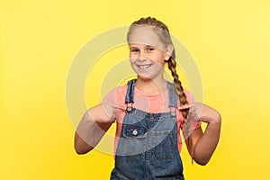 This is me! Portrait of cheerful confident little girl in denim overalls pointing herself, selfishly paying attention to own