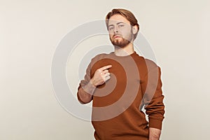 This is me! Portrait of egoistic arrogant selfish man with beard in sweatshirt pointing himself, gray background