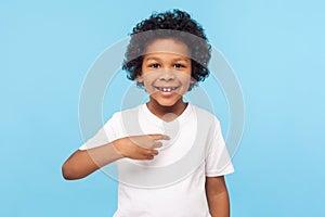 This is me. Portrait of happy preschool curly boy in T-shirt joyfully looking at camera and pointing to himself