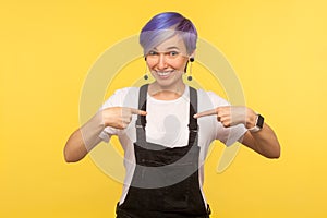 This is me! Portrait of joyful hipster woman pointing herself, smiling and expressing pride. yellow background studio shot