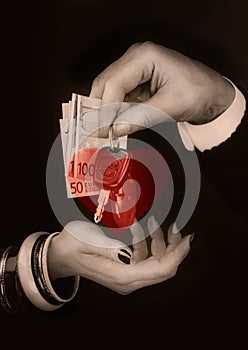 Me`s hand giving to  woman`s hand euro banknotes and car keys in front of transparent red heart shape