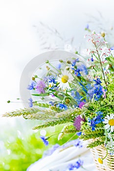 Meadow colorful flowers bouquet in wicker basket on nature background outdoors on white tablecloth