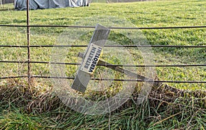 meadow with fence and a tipped over sign showing the german words \