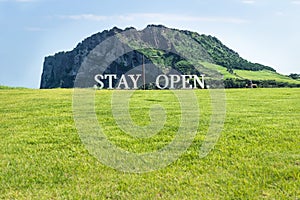 Meadow with the sign `stay open` with Ilchulbong in the background, Seongsan, Jeju Island, South Korea