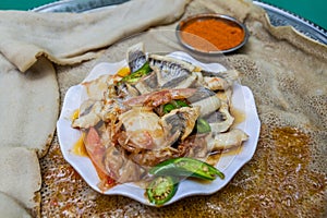 Meal in Ethiopia - pieces of fish with chilli peppers and vegetables on injera flat bre