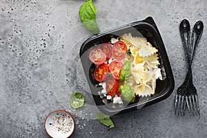 Meal prep. Black lunch boxes. Pasta bows, cherry tomatoes, young cheese, salt, pepper, basil. On a dark background Top