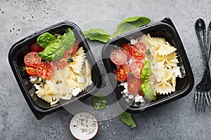 Meal prep. Black lunch boxes. Pasta bows, cherry tomatoes, young cheese, salt, pepper, basil. On a dark background Top