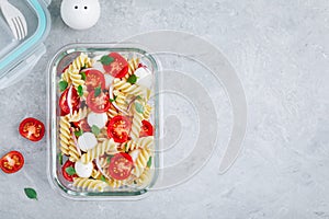 Meal prep containers with pasta salad, tomatoes, mozzarella cheese, red onion and basil