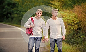 means of travel. twins walking along road. two brothers go adventure. friendship. men hitch hiking. man casual style