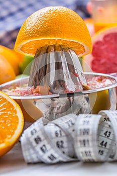 Measure tape and juicer with citrus fruits. Preparation of orange grape or multivitamin juice, hands squeeze juice on a manual me