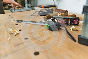Measure tape, mallet, wood filings, and other necessary tools used carpentry lying on wooden table. Carpenter hands in