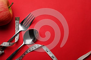 Measure tape, spoon fork and apple on red background. Loss weight and healthy diet concept.