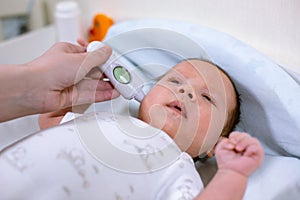 Measuring baby`s temperature with contactless thermometer. Mom measures the baby`s body temperature with a thermometer