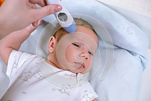 Measuring baby`s temperature with contactless thermometer. Mom measures the baby`s body temperature with a thermometer