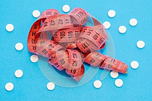 Measuring centimeter tape is on blue background surrounded by white round tablets. Concept photo pharmacological weight loss and