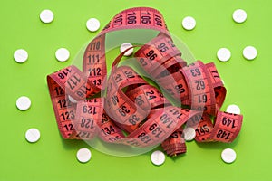 Measuring centimeter tape is on greenbackground surrounded by white round tablets. Concept photo pharmacological weight loss and u