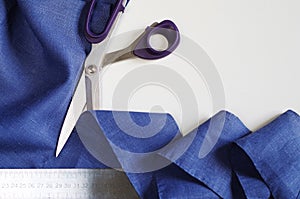Measuring and cutting textile. Scissors and violet linen fabric.