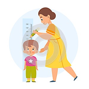 Measuring height. Mom helps her son measure growth, makes mark with pencil, wall-mounted kids meter, little boy standing