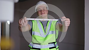Measuring roulette tape in male hands with blurred man smiling at background looking at camera. Happy confident