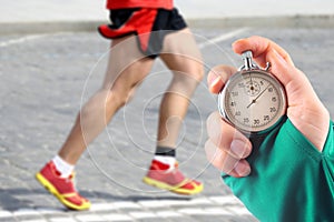 Measuring the running speed of an athlete using a mechanical stopwatch. hand with a stopwatch on the background of the legs of a