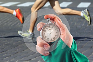 Measuring the running speed of an athlete using a mechanical stopwatch. hand with a stopwatch on the background of the legs of a