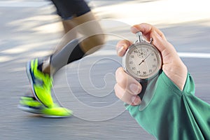 Measuring the running speed of an athlete using a mechanical stopwatch. hand with a stopwatch on the background of the legs of a