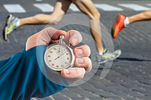 Measuring the running speed of an athlete using a mechanical stopwatch. hand with a stopwatch on the background of the legs of a