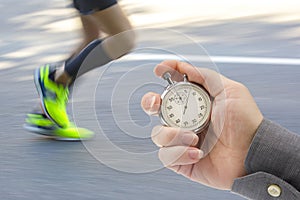 Measuring the running speed of an athlete using a mechanical stopwatch. hand with a stopwatch on the background of the legs of a