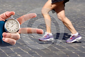 Measuring the running speed of an athlete using a mechanical stopwatch. hand with a stopwatch on the background of the legs of a