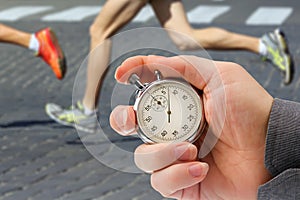 Measuring the running speed of an athlete using a mechanical stopwatch. hand with a stopwatch on the background of the legs of a