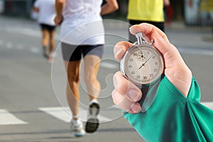 Measuring the running speed of an athlete using a mechanical stopwatch. hand with a stopwatch on the background of the legs of a